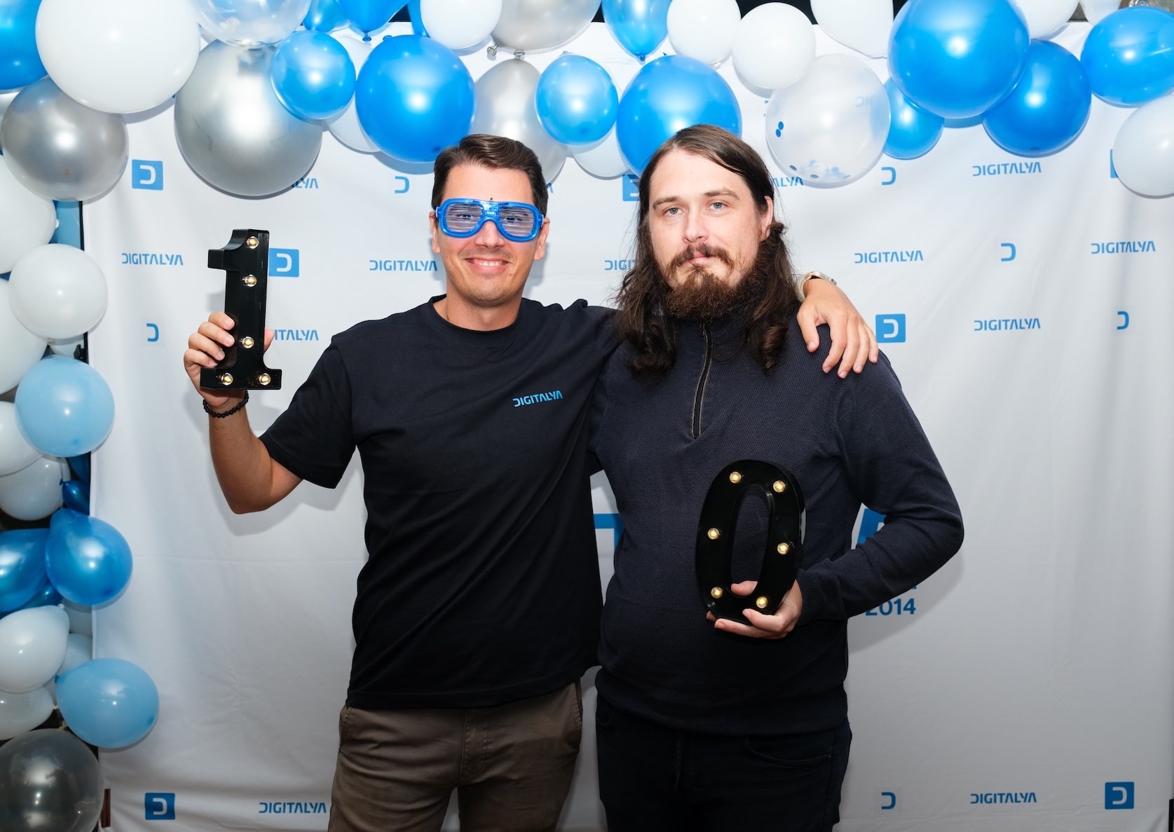 Ovidiu and Marius smiling, posing with marquee letter lights "D" and "J," against a backdrop of blue and white balloons.